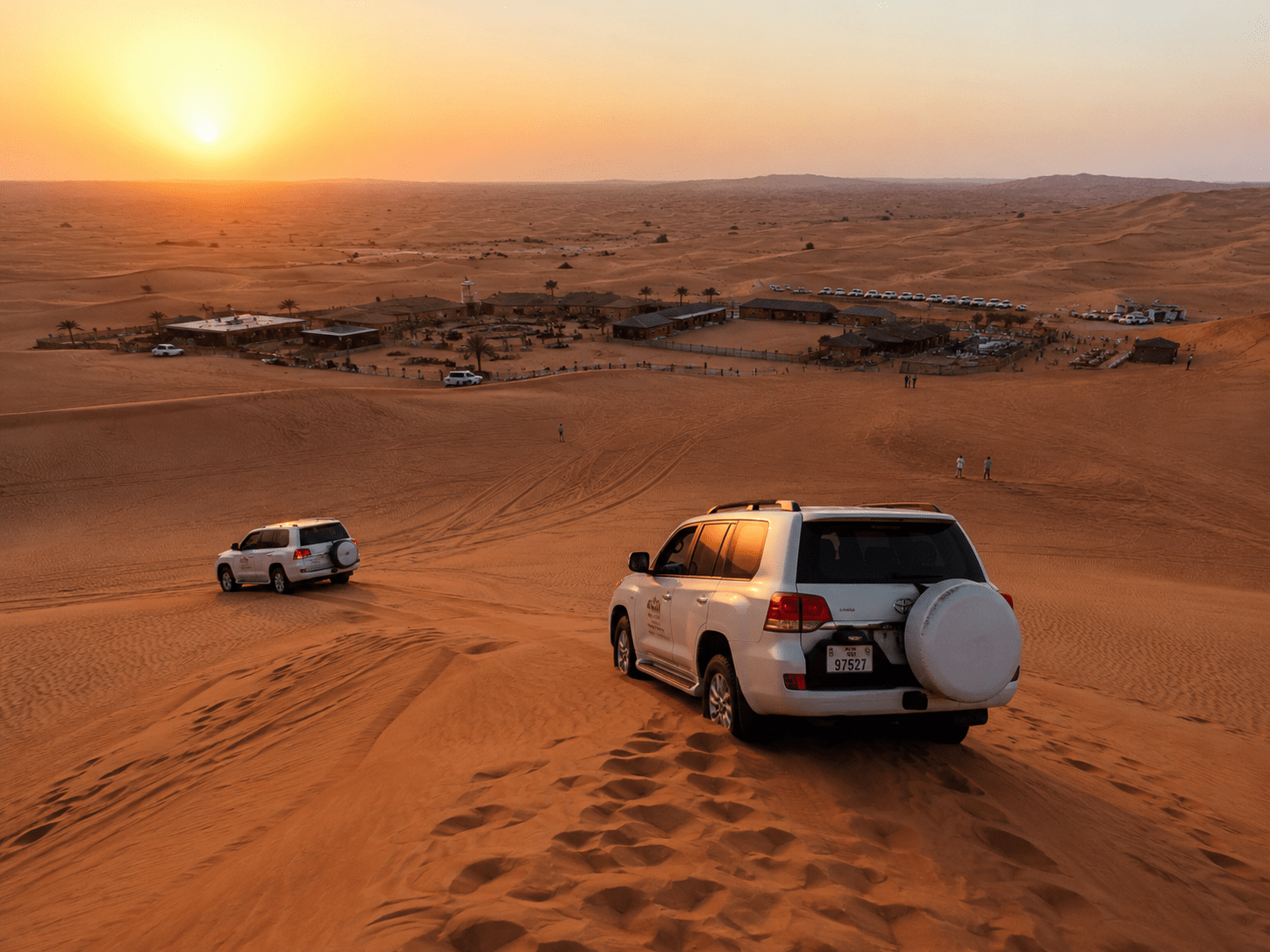"White 4x4 SUVs dune bashing during a desert safari Dubai tour at sunset