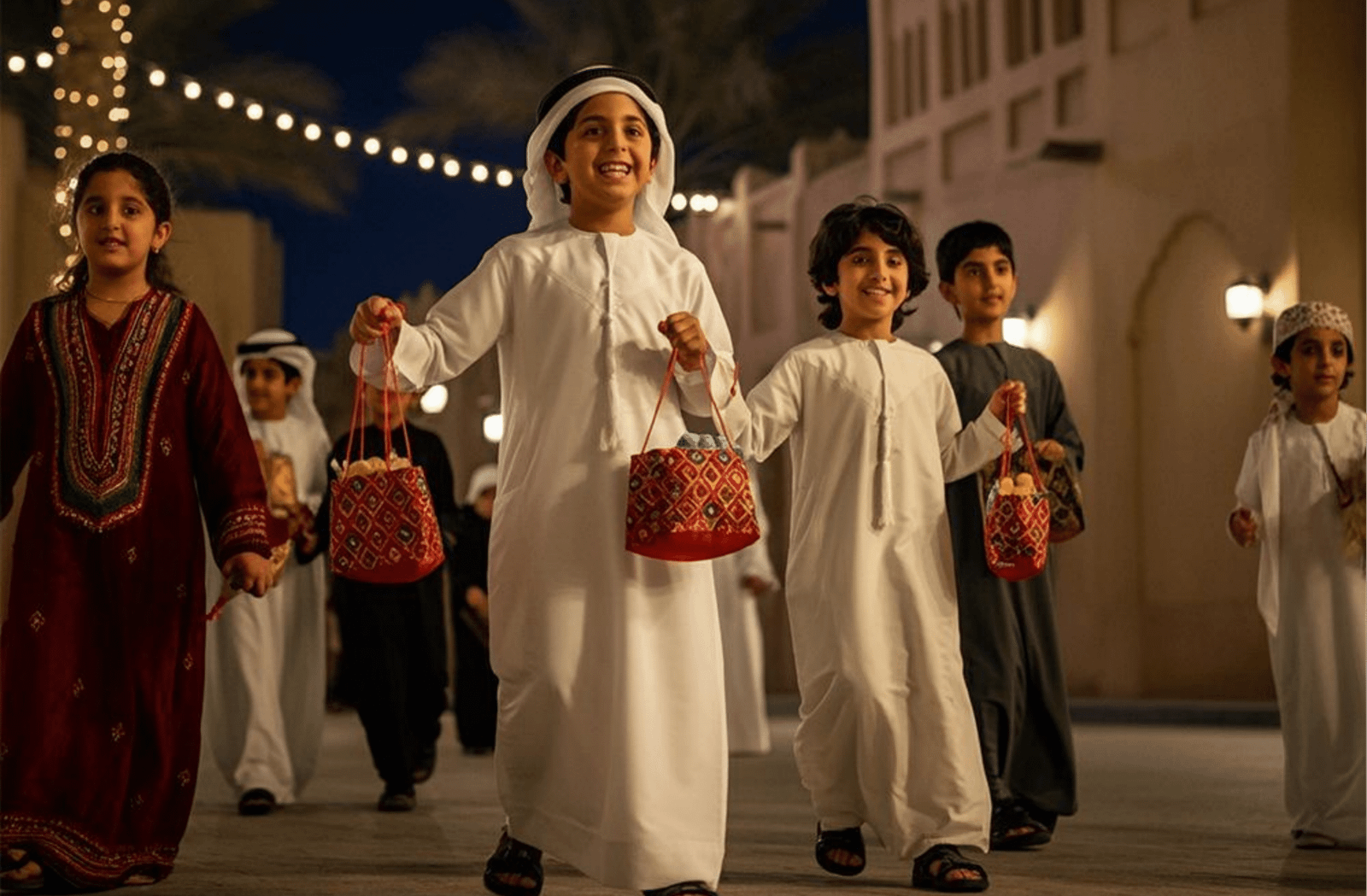 Children in traditional Arabian clothing stroll down a vibrant street, showcasing cultural attire and community spirit.