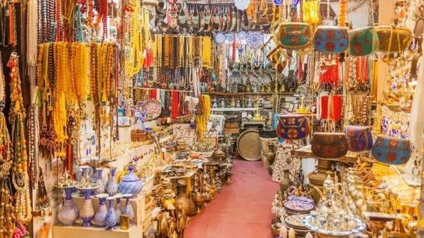 Busy Rolla Market Sharjah street with traditional clothes, gold jewellery, spices, perfumes, and shoppers in local market shops.